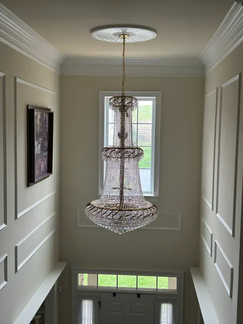 Two-story foyer with crystal chandelier, wainscoting panel molding, and fresh paint