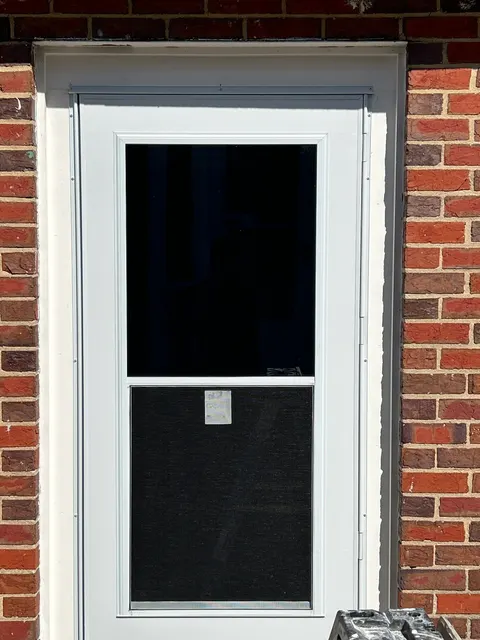 Completed exterior entry with new storm door and white trim in brick opening