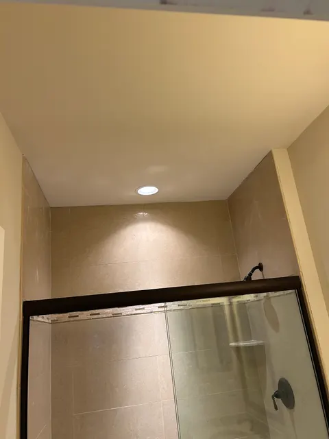 Completed walk-in shower with beige stone tile, glass enclosure, and bronze rain fixtures