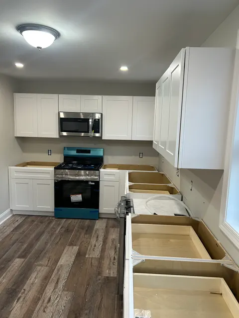 White shaker kitchen cabinets and range wall being fitted with new stainless appliances
