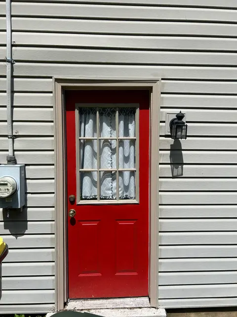 Red side entry door framed by new tan vertical siding and lantern light