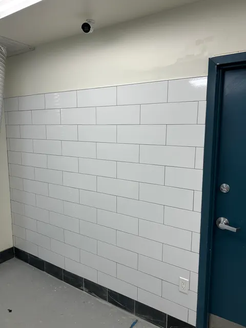 Glossy white vertical tile wall with integrated outlet beside navy blue door