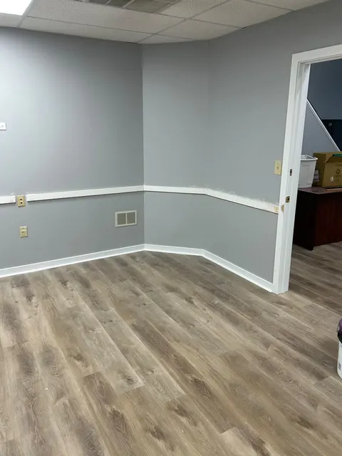 Corner detail of new baseboards, chair rail and gray luxury vinyl plank flooring meeting a painted door casing