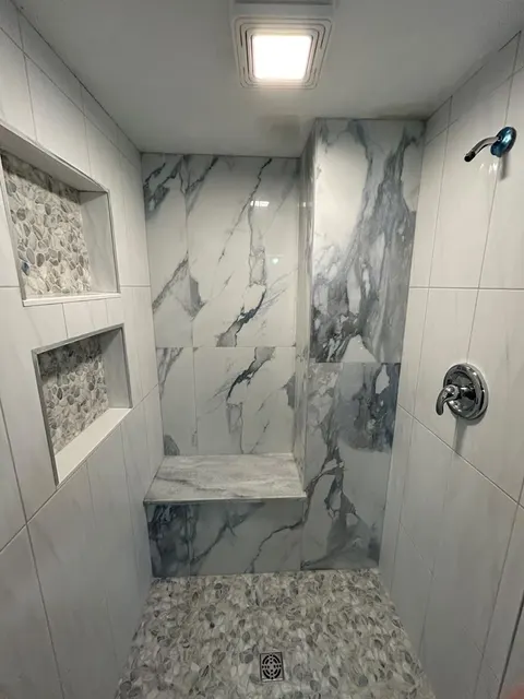 Walk-in shower with river-pebble floor, built-in quartz bench, two recessed niches and a marble-look porcelain accent wall