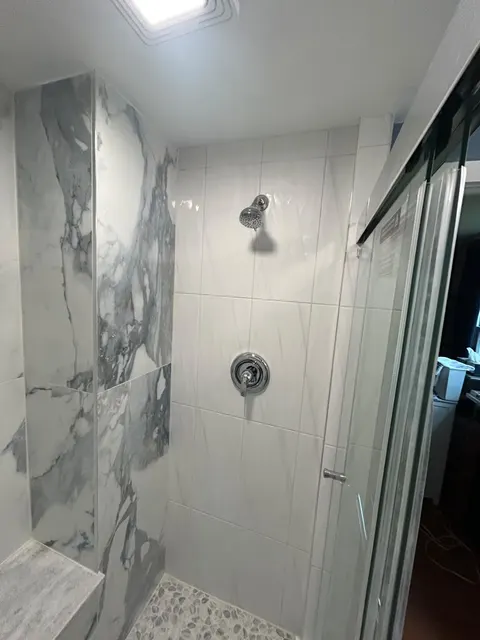 Shower valve wall in large white porcelain tile next to a marble-look accent column and tiled bench